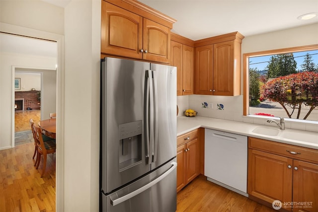 kitchen with white dishwasher, a sink, light wood-style floors, light countertops, and stainless steel refrigerator with ice dispenser