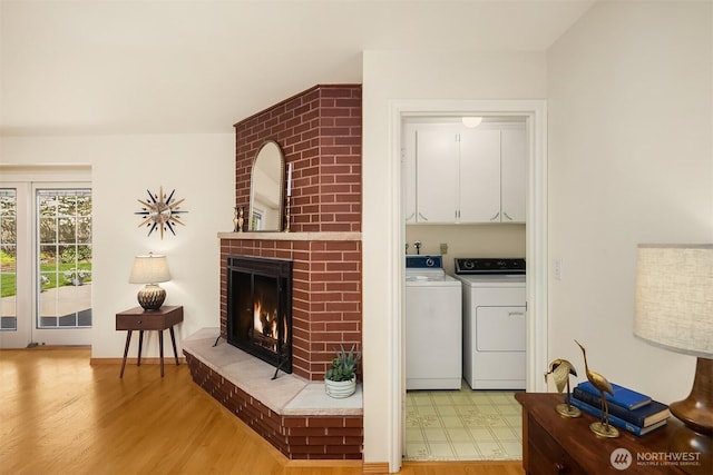 living room with washing machine and clothes dryer, a brick fireplace, and light wood-style flooring