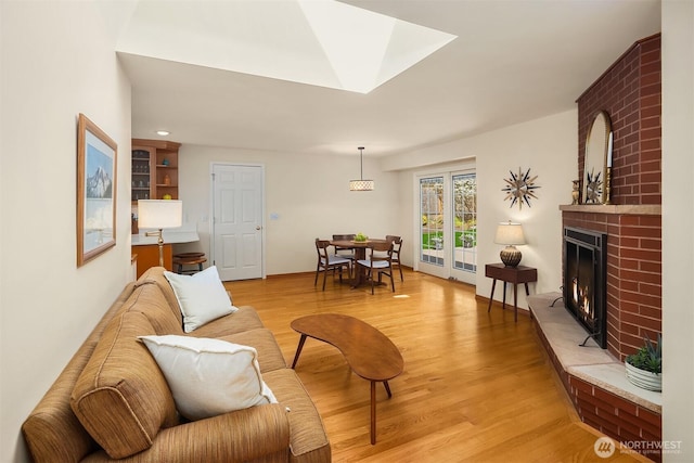 living area featuring light wood-style floors, a skylight, and a brick fireplace