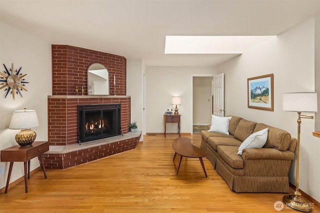 living room featuring baseboards, a brick fireplace, wood finished floors, and a skylight
