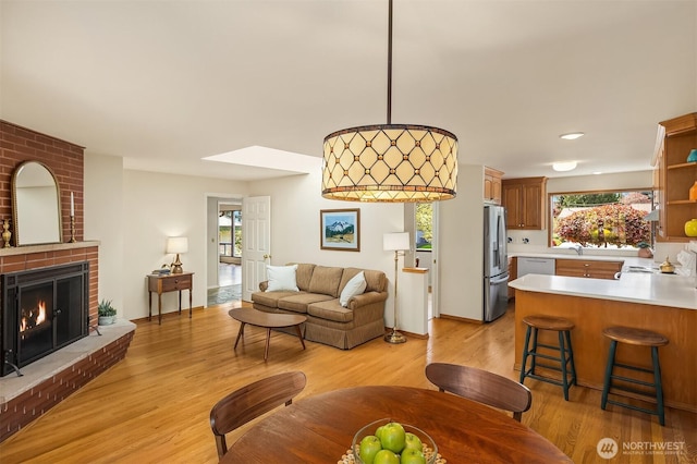 living room with light wood-style flooring, a brick fireplace, and a skylight