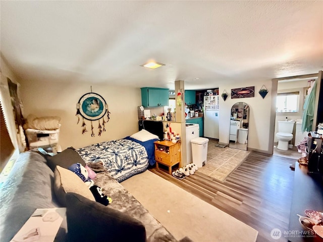 bedroom with light wood-type flooring, ensuite bathroom, and freestanding refrigerator