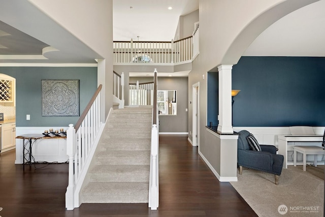 stairs with arched walkways, decorative columns, and wood finished floors