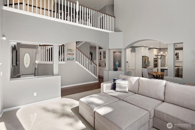 living area featuring an inviting chandelier, arched walkways, baseboards, a towering ceiling, and stairway