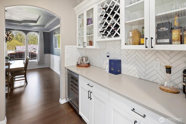 bar featuring wainscoting, a dry bar, arched walkways, dark wood finished floors, and wine cooler