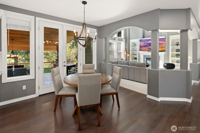 dining room with a glass covered fireplace, baseboards, dark wood-style floors, arched walkways, and a notable chandelier