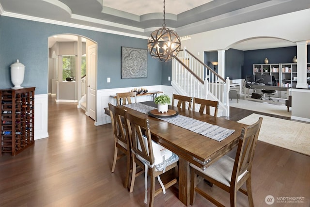 dining room with arched walkways, wainscoting, wood finished floors, and a raised ceiling