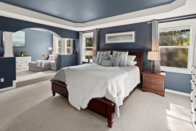 bedroom with decorative columns, baseboards, light colored carpet, a raised ceiling, and arched walkways