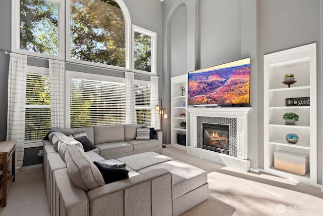 carpeted living room with a towering ceiling, a glass covered fireplace, and built in shelves