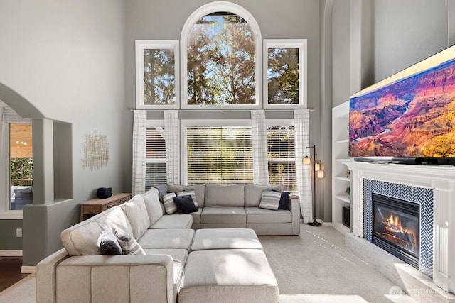 living room featuring arched walkways, a high ceiling, a fireplace, and carpet floors
