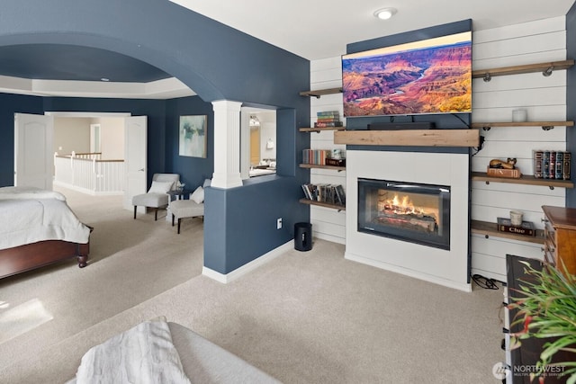 bedroom with arched walkways, baseboards, a glass covered fireplace, carpet, and ornate columns