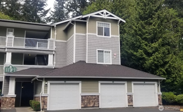 view of front facade with stone siding, a balcony, and asphalt driveway