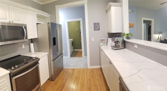 kitchen featuring appliances with stainless steel finishes, light wood-style floors, white cabinetry, light stone countertops, and washer / clothes dryer