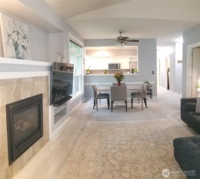 carpeted dining area featuring a ceiling fan, a tiled fireplace, and baseboards