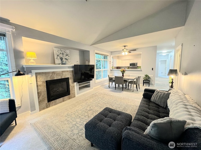 living room with carpet floors, baseboards, a tile fireplace, lofted ceiling, and ceiling fan