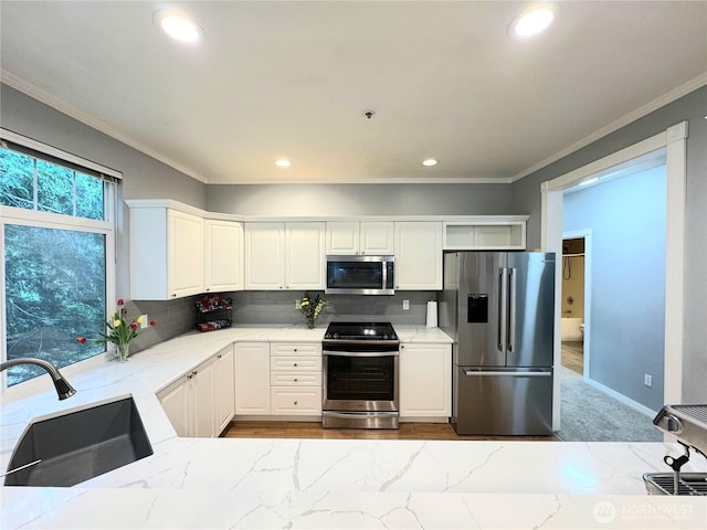 kitchen with appliances with stainless steel finishes, a sink, light stone countertops, crown molding, and decorative backsplash