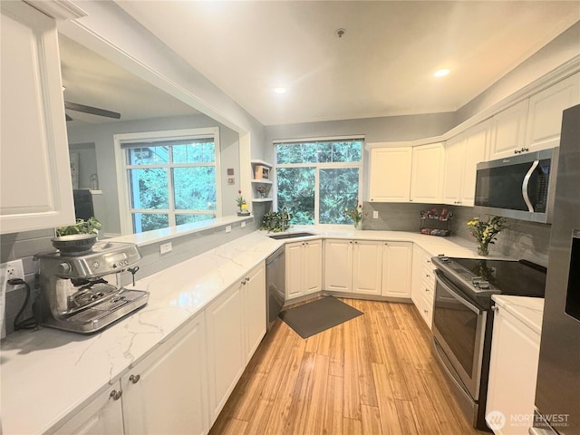 kitchen with stainless steel appliances, a sink, white cabinetry, tasteful backsplash, and light wood finished floors