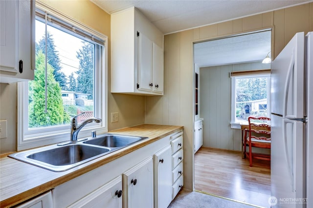 kitchen with light wood-type flooring, a sink, light countertops, white cabinets, and freestanding refrigerator