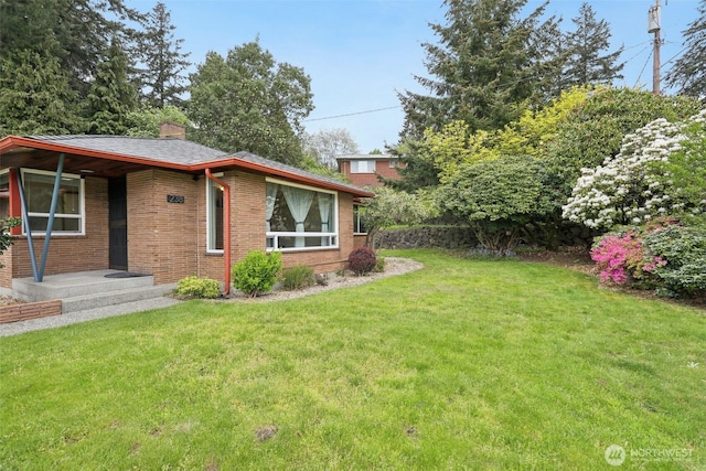 exterior space with brick siding, a yard, and a chimney