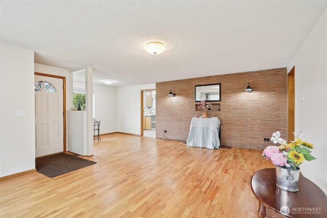 foyer entrance with a textured ceiling, brick wall, baseboards, and light wood-style floors
