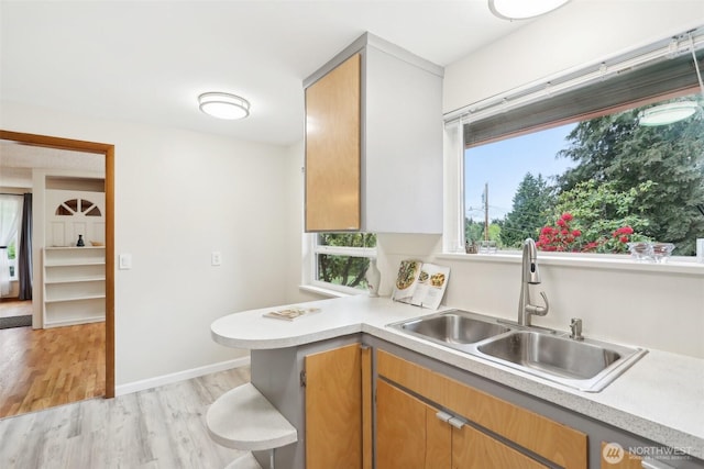kitchen with light countertops, a peninsula, a sink, and light wood finished floors