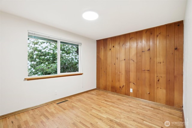 empty room featuring wooden walls, baseboards, visible vents, and wood finished floors