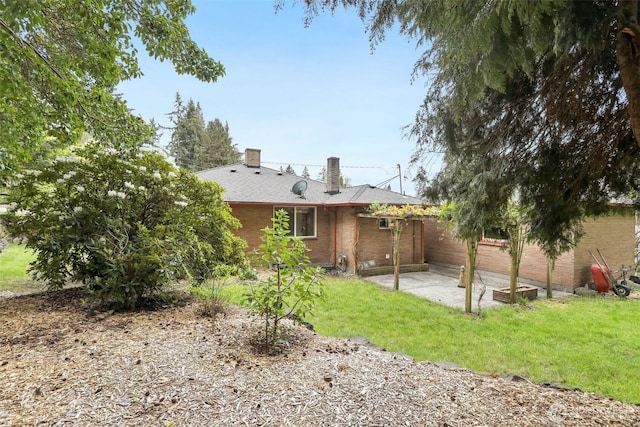back of property featuring a lawn, a chimney, a patio area, and brick siding