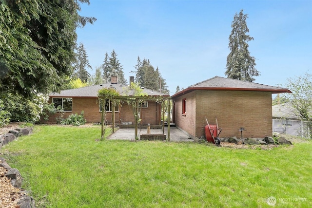 back of property with a lawn, brick siding, a patio area, and a chimney