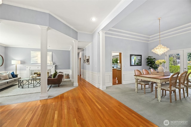 dining area featuring ornamental molding, decorative columns, a wainscoted wall, light wood finished floors, and a premium fireplace