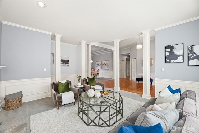 living area with crown molding, carpet flooring, decorative columns, and a wainscoted wall