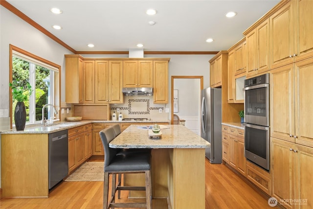 kitchen featuring a kitchen island, crown molding, a sink, under cabinet range hood, and stainless steel appliances