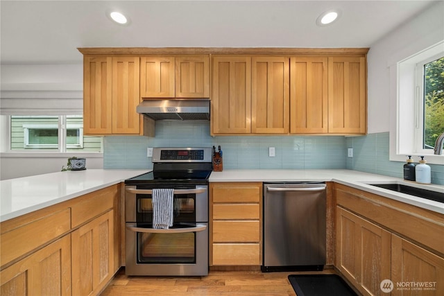 kitchen with under cabinet range hood, appliances with stainless steel finishes, tasteful backsplash, and light countertops