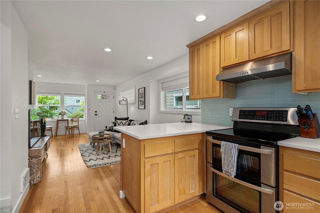 kitchen with range with two ovens, a peninsula, decorative backsplash, light wood-type flooring, and under cabinet range hood