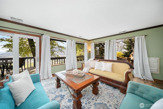 living room with crown molding, visible vents, a healthy amount of sunlight, and wood finished floors