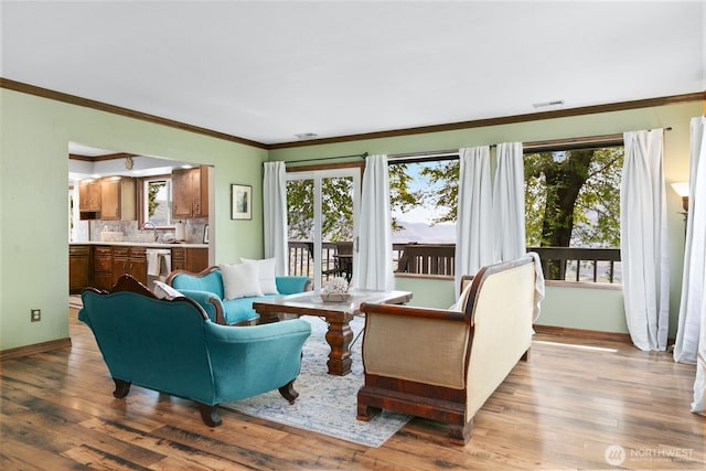 living area with baseboards, ornamental molding, wood finished floors, and visible vents