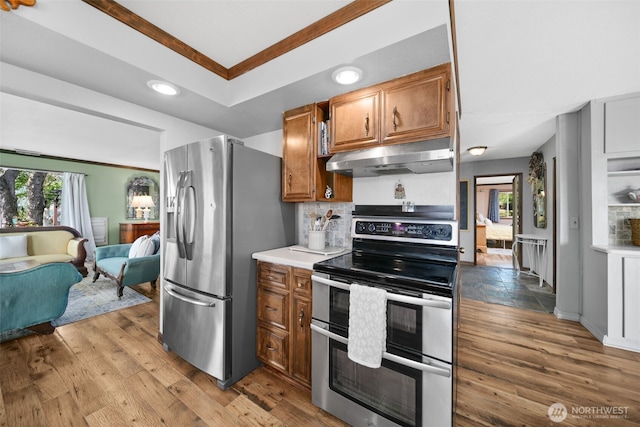 kitchen with crown molding, recessed lighting, under cabinet range hood, brown cabinets, and appliances with stainless steel finishes