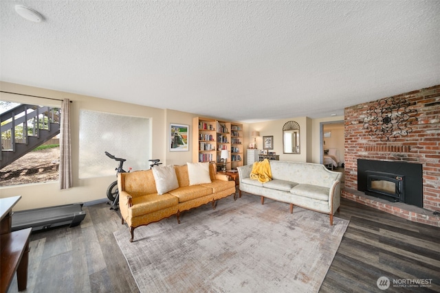 living area with a brick fireplace, a textured ceiling, wood finished floors, and stairway