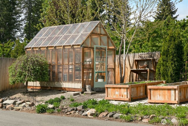 view of greenhouse with fence and a vegetable garden