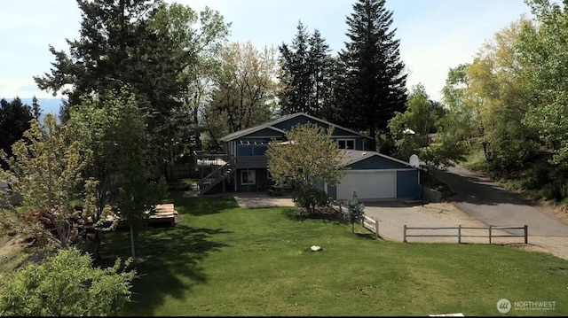 view of property hidden behind natural elements with driveway, a front yard, a garage, stairway, and fence