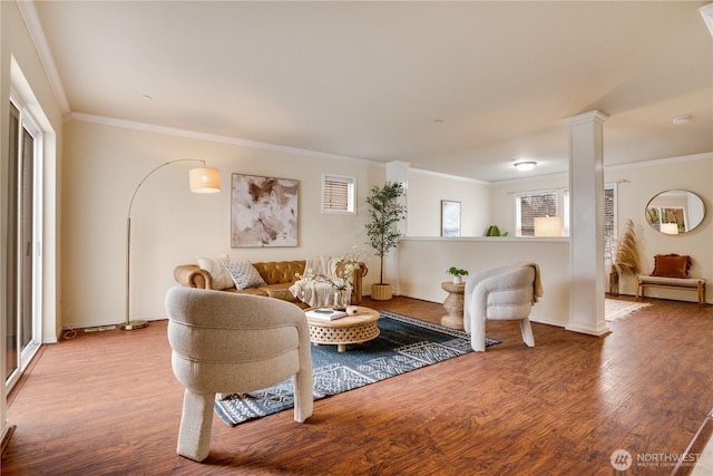 living area featuring baseboards, ornate columns, wood finished floors, and crown molding