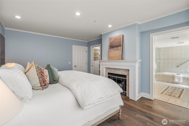 bedroom with crown molding, a fireplace, dark wood-style floors, connected bathroom, and recessed lighting