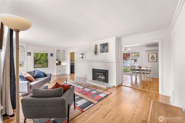 living area with a brick fireplace, an AC wall unit, a chandelier, baseboards, and light wood-type flooring