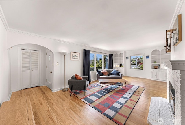 living room featuring arched walkways, a fireplace, baseboards, ornamental molding, and light wood-style flooring
