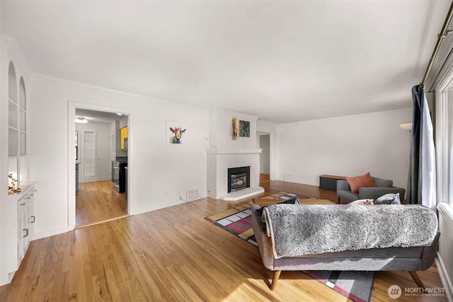 living room featuring visible vents, light wood finished floors, and a brick fireplace