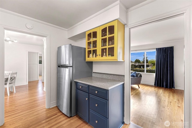 kitchen with crown molding, glass insert cabinets, freestanding refrigerator, and light wood-style floors