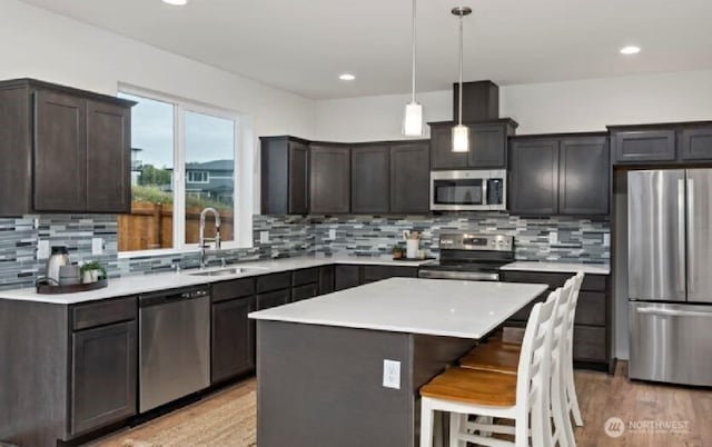 kitchen with a sink, light countertops, a kitchen breakfast bar, stainless steel appliances, and light wood-type flooring