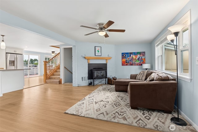 living area with a ceiling fan, stairs, a glass covered fireplace, and wood finished floors