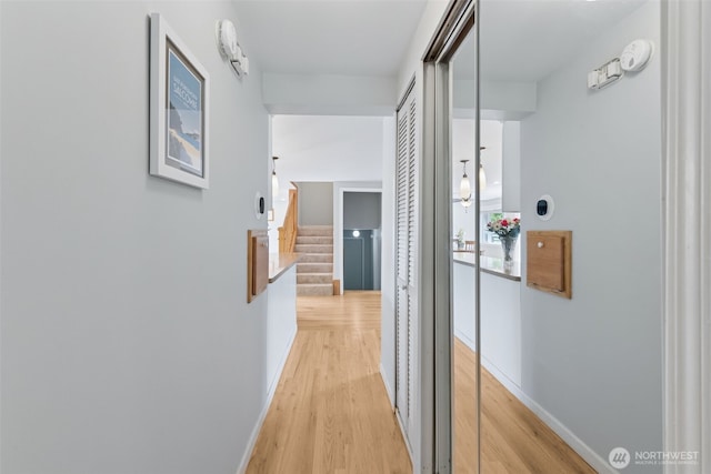 corridor with light wood-style floors, baseboards, and stairway