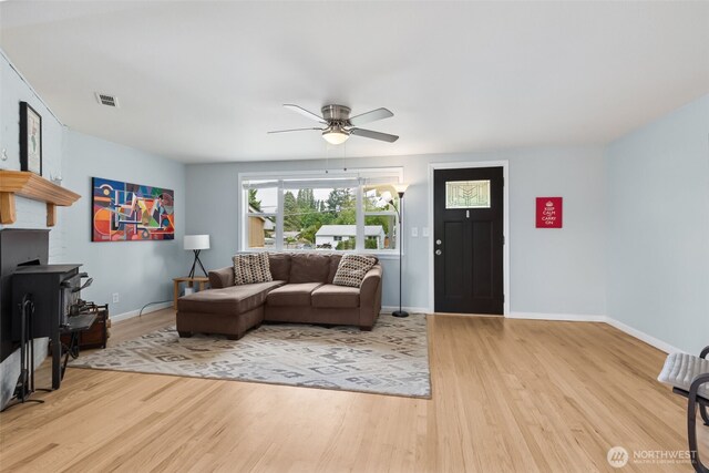 living room featuring light wood-type flooring, baseboards, a ceiling fan, and a wood stove