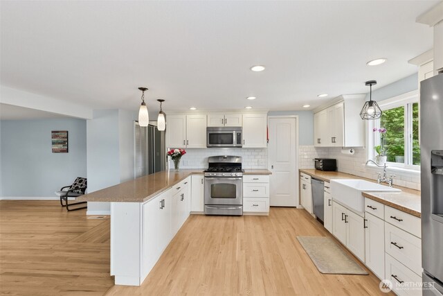 kitchen with stainless steel appliances, a sink, a peninsula, light wood-style floors, and recessed lighting